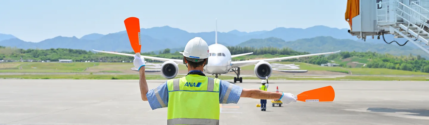 滑走路で地上スタッフに誘導されるANAの旅客機
